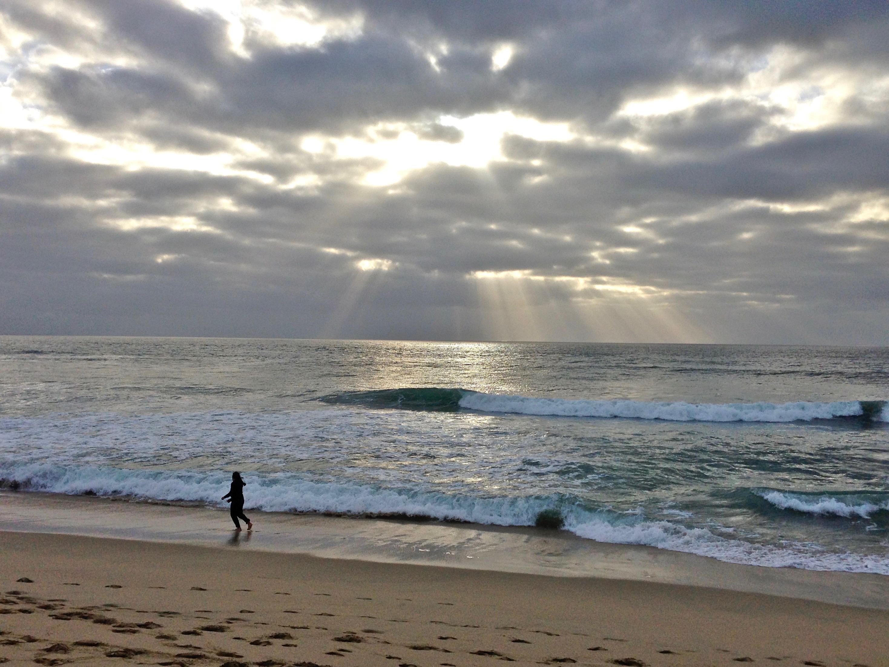 A beach walker at Half Moon Bay State Beach is accentuated by sunlight bursting through the clouds. 